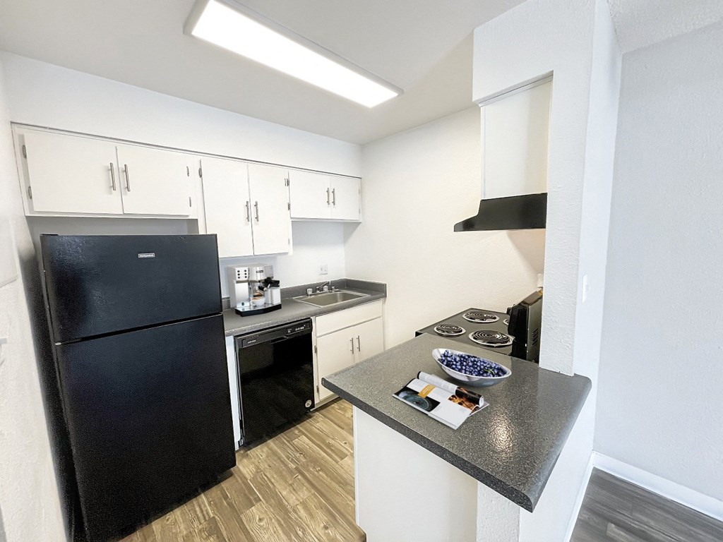 A black refrigerator is in a kitchen with white walls.